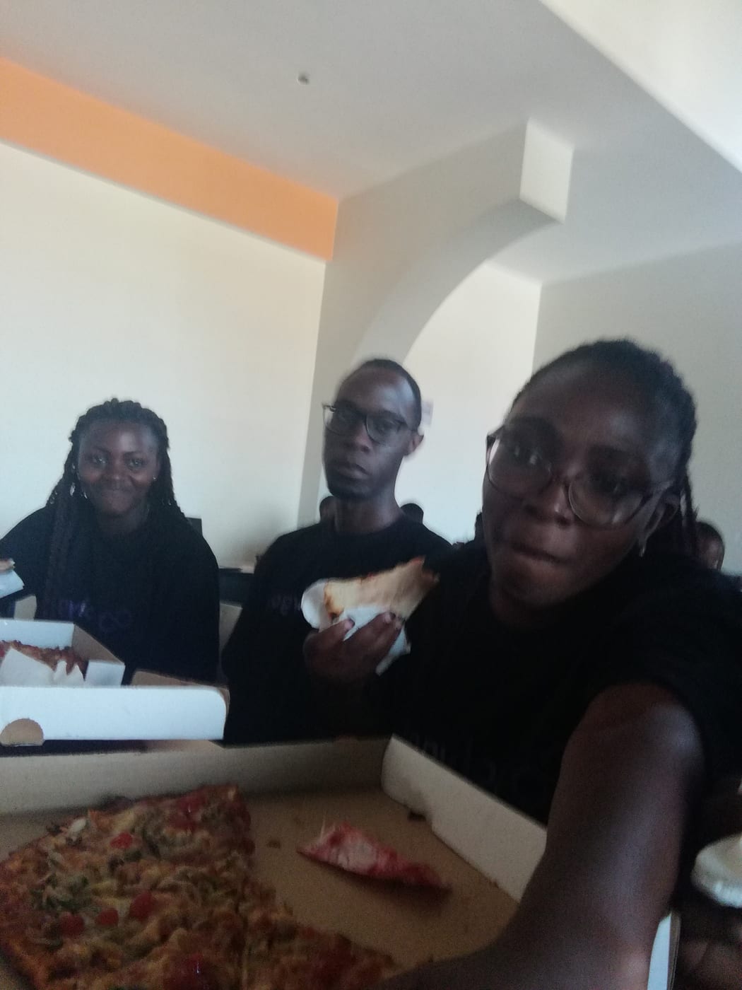 Three attendees in black event shirts sharing pizza during a break.