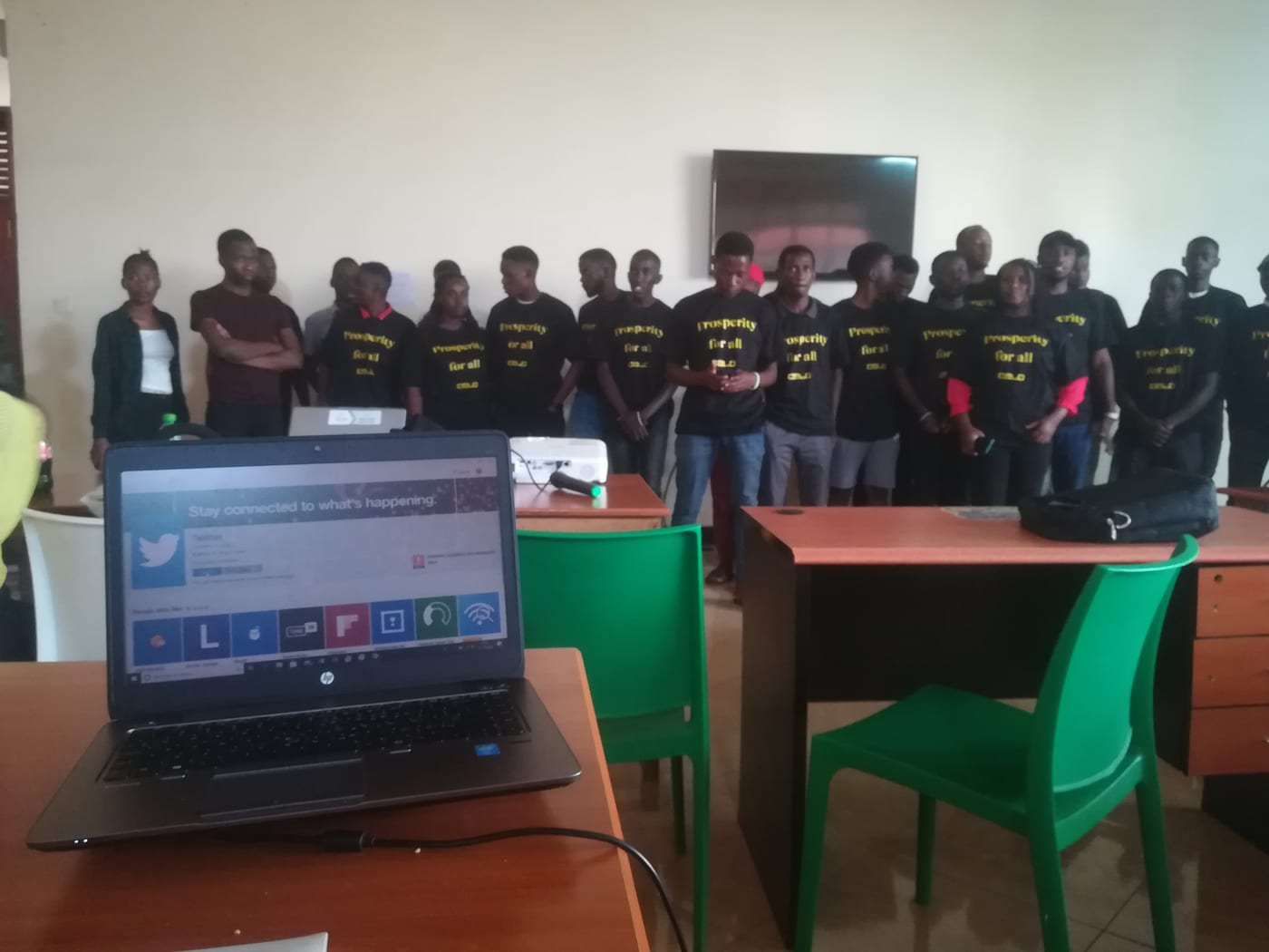 Attendees in matching black "Prosperity for all" T-shirts standing at the front of the room, with a presentation laptop in the foreground.